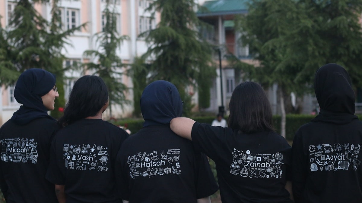 Five people in black t-shirts with white designs outdoors.