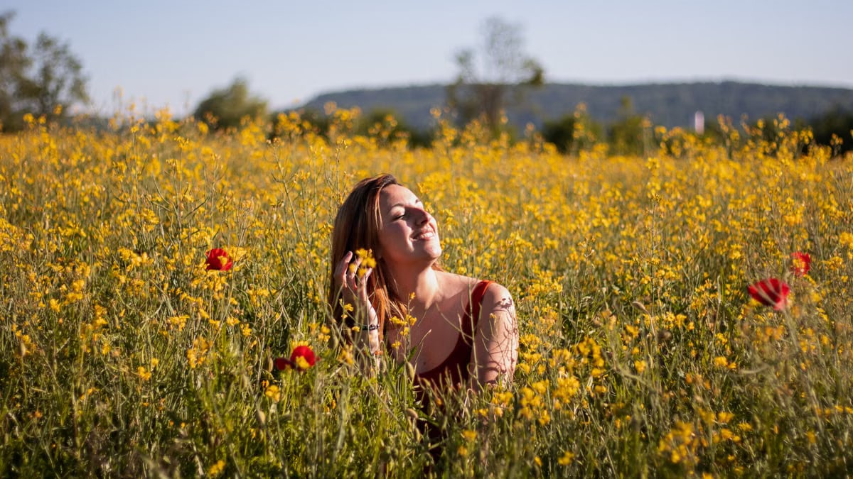 A woman sits with eyes closed, enjoying the sun in a vibrant yellow flower field.